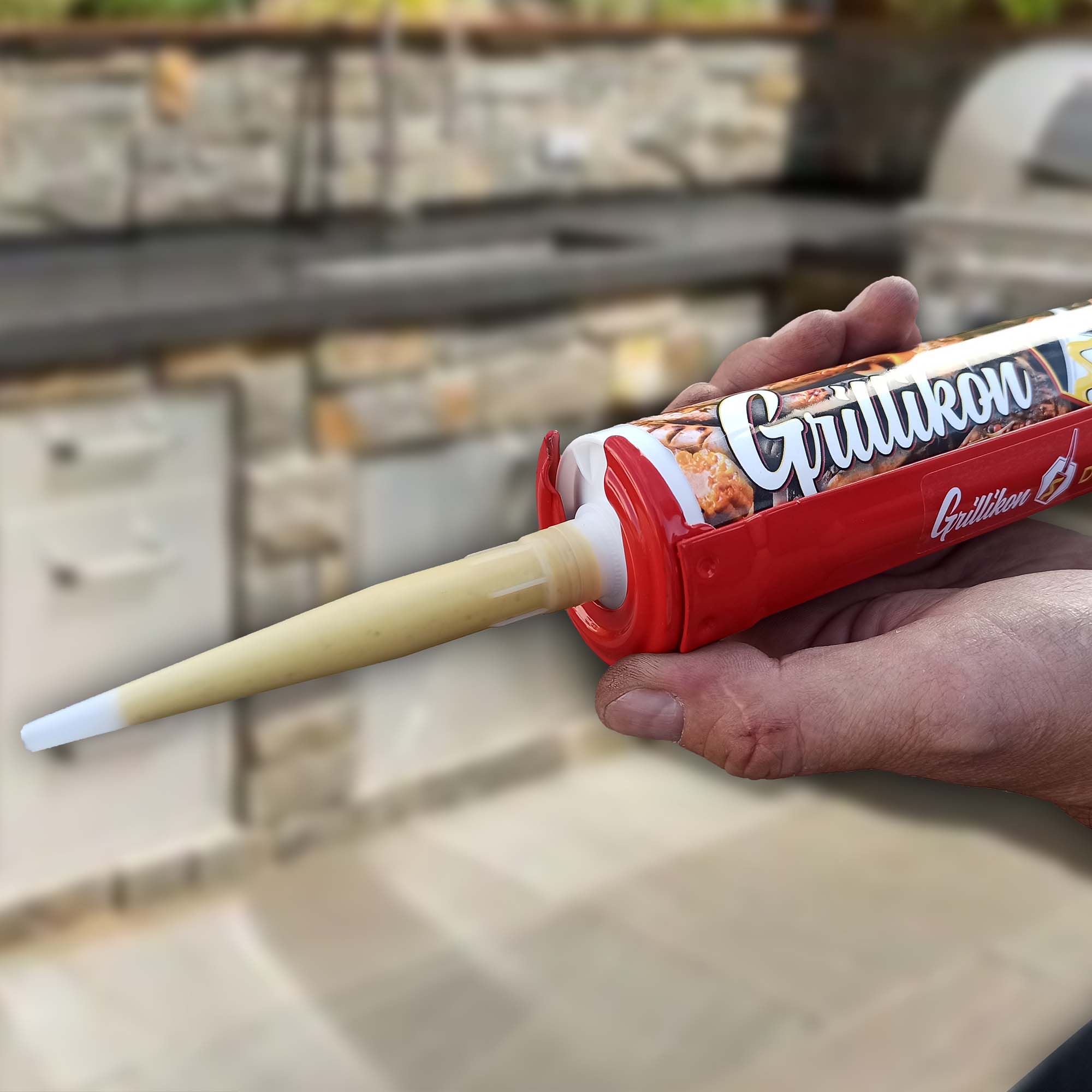 Hand hält Grillikon Kartuschenpistole mit 300 ml Grillsoßen-Kartusche aus dem Geschenkset „WM-Edition“ mit 3x Mix und Grillschürze