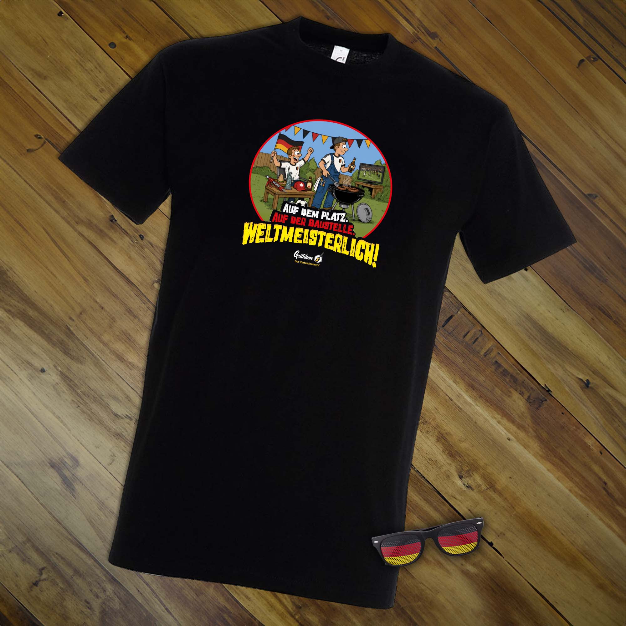 Schwarzes WM-T-Shirt aus dem Grillikon Geschenkset „WM-Edition“ mit Fußball-Grillmotiv und Fanbrille in Deutschlandfarben neben dem Shirt