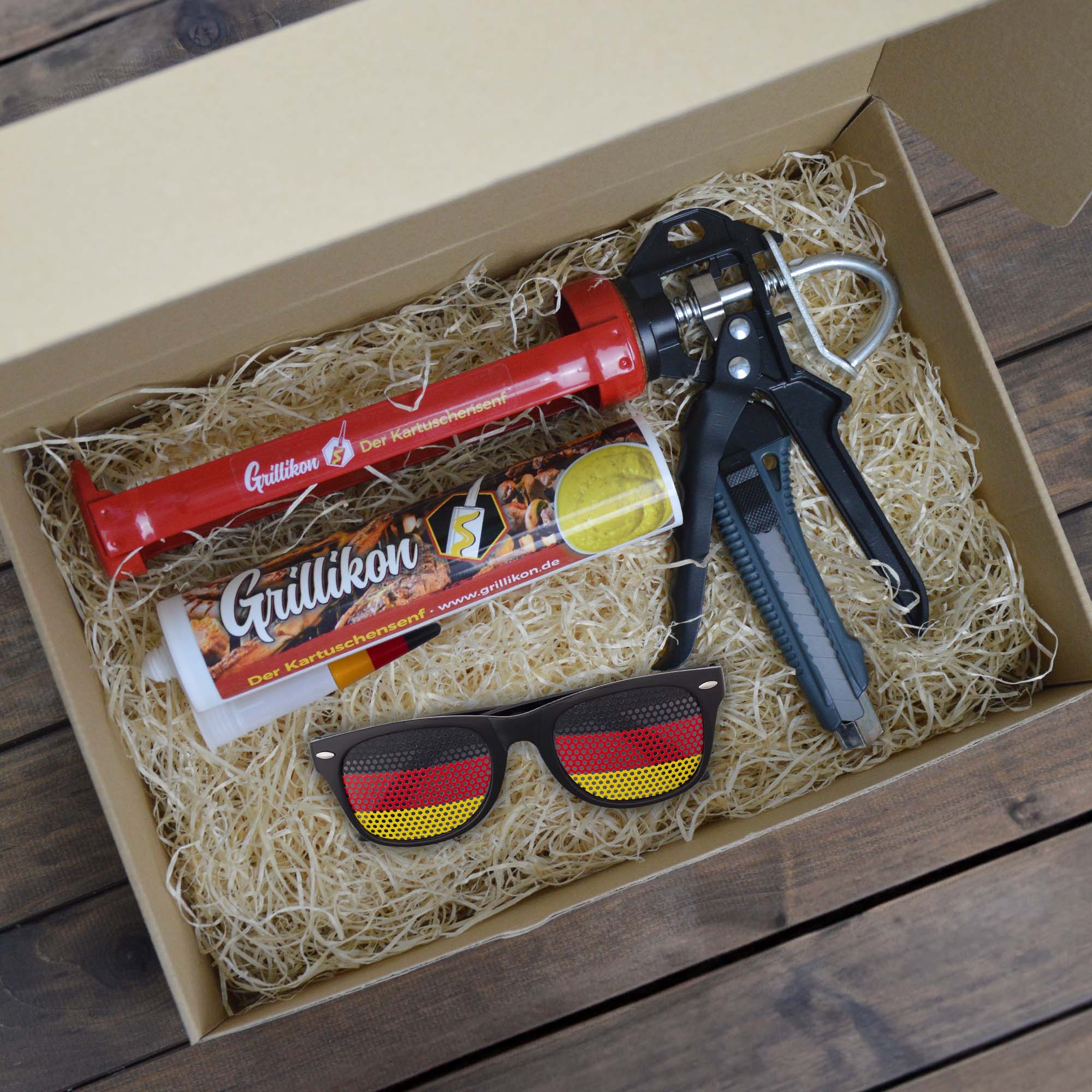 Grillikon Geschenkset „WM-Edition“ mit mittelscharfem Senf in 300 ml Kartusche, Kartuschenpistole, Cuttermesser und Deutschland-Fanbrille im Geschenkkarton mit Holzwolle